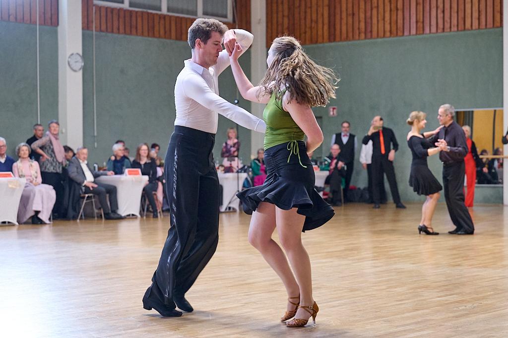 Tanzpaar in eleganter Tanzhaltung auf einer Tanzfl&auml;che, Zuschauer sitzen an Tischen im Hintergrund.