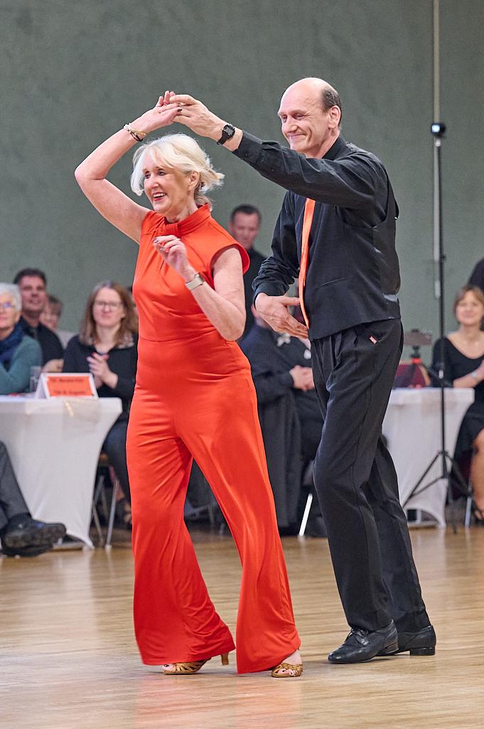 Tanzendes Paar in eleganter Kleidung auf einer Tanzfl&auml;che, umgeben von Zuschauern bei einem Wettbewerb.