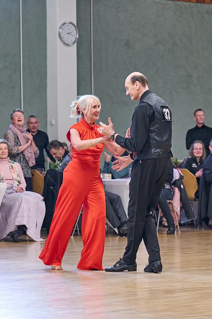 Tanzpaar in eleganter Kleidung steht auf der Tanzfl&auml;che und l&auml;chelt sich an, im Hintergrund Zuschauer an Tischen.