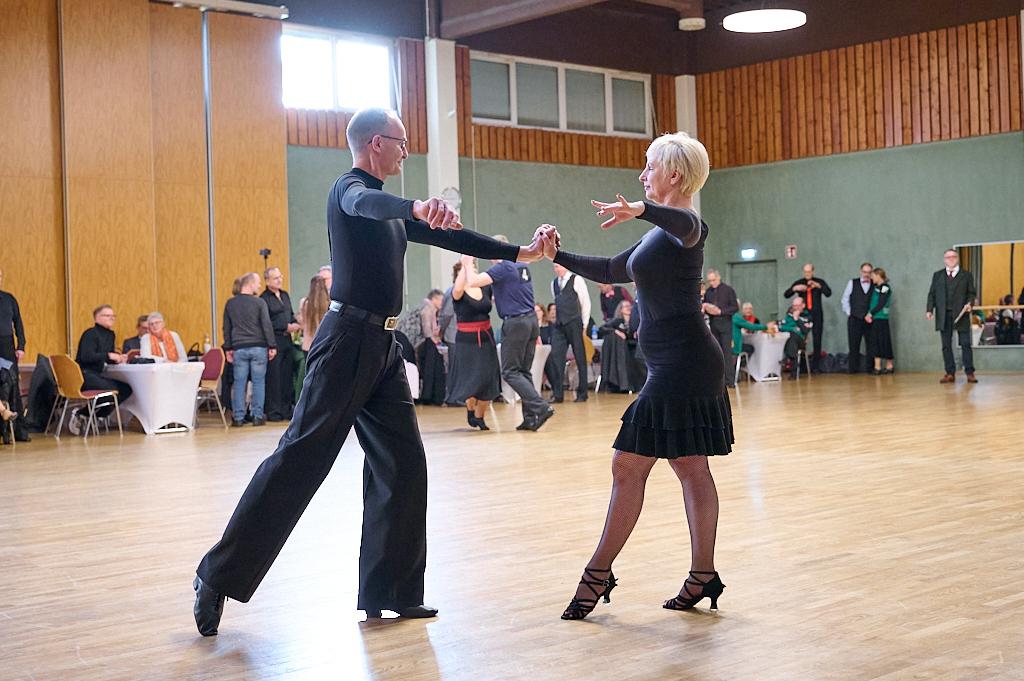 Tanzpaar bewegt sich elegant auf einer Tanzfl&auml;che, umgeben von Zuschauern in einem festlichen Saal.