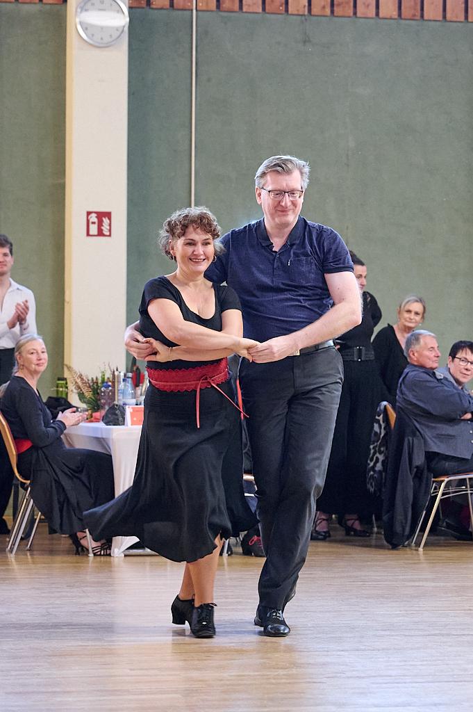 Tanzender Mann und Frau in eleganter Kleidung auf einer Tanzfl&auml;che, umgeben von applaudierendem Publikum.