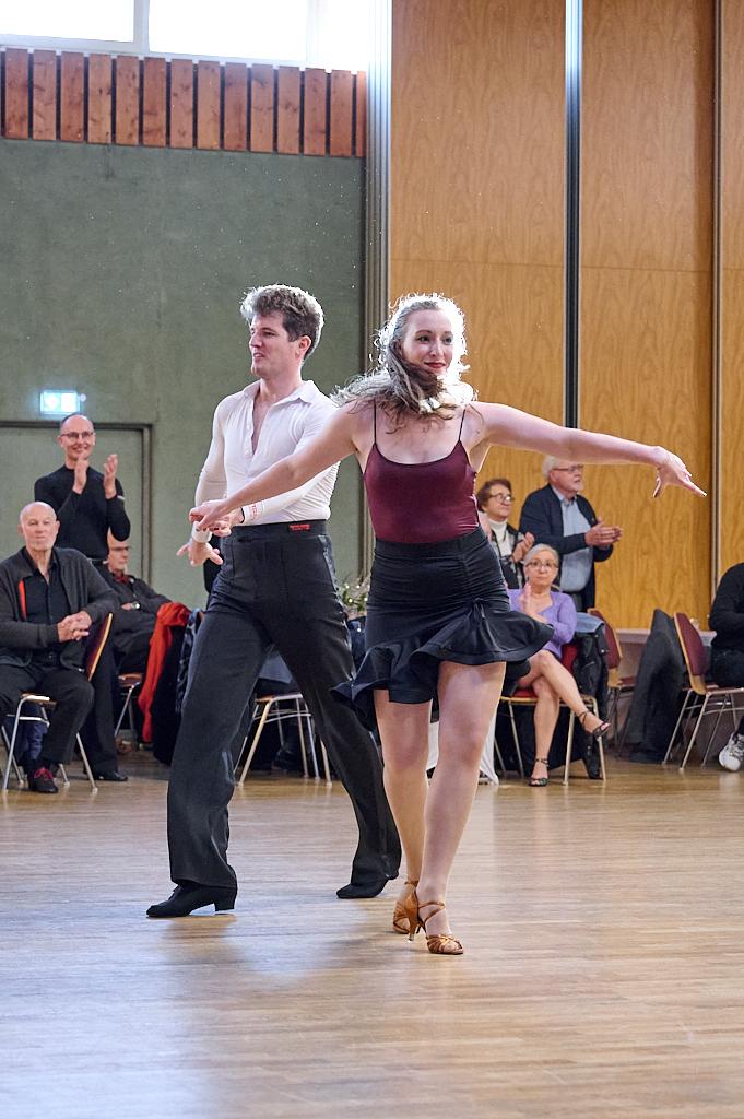 Tanzpaar in eleganter Kleidung f&uuml;hrt einen Tanz vor Publikum in einer hellen Sporthalle auf.