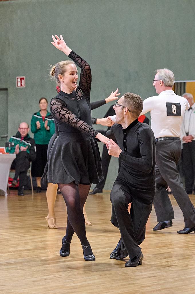 Tanzpaar in formeller Kleidung, w&auml;hrend eines Tanzwettbewerbs auf Holzfl&auml;che, Publikum im Hintergrund.