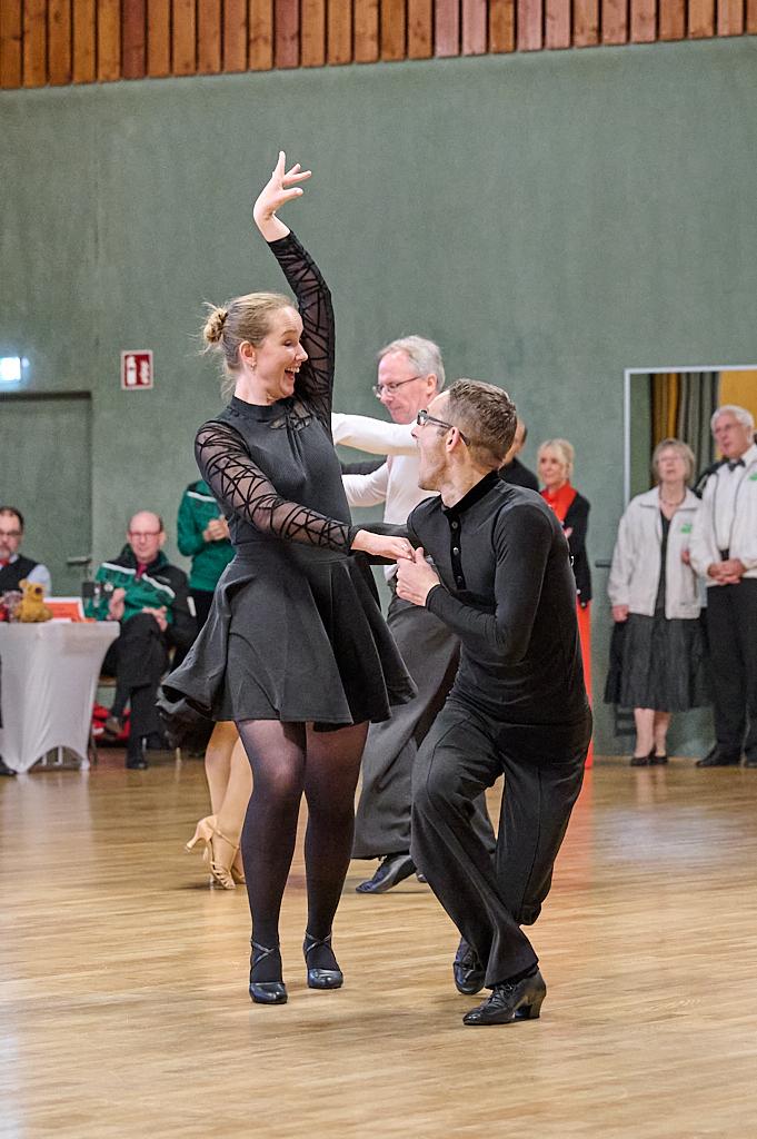 Tanzende Paare in eleganter Kleidung bei einer Veranstaltung in einer h&ouml;lzernen Halle. Die Stimmung ist lebhaft.