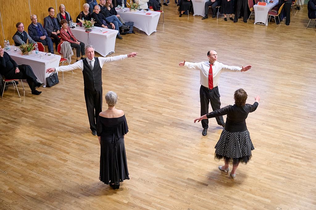Tanzpaar zeigt eine Choreografie auf einer Holztanzfl&auml;che, umgeben von aufmerksam zuschauendem Publikum.