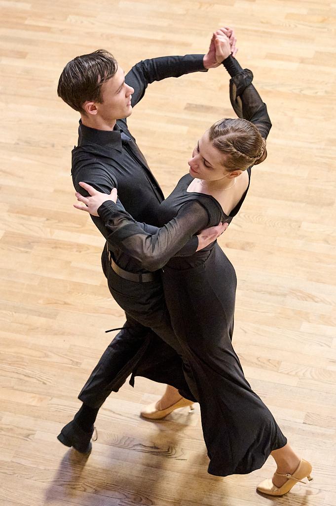 Paar in eleganter Tanzkleidung tanzt eng umschlungen auf einem Holzfu&szlig;boden.