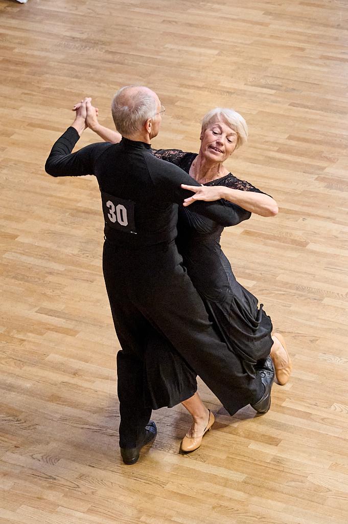 Tanzendes Paar in eleganter Kleidung auf einem Holzboden, Frau mit leicht frisiertem Haar l&auml;chelt.