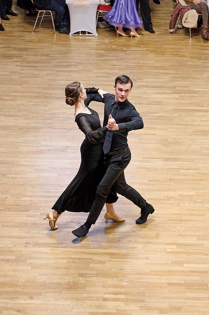 Tanzpaar in eleganter Abendkleidung f&uuml;hrt einen Ausdruckstanz auf einer Holzfl&auml;che vor Publikum aus.