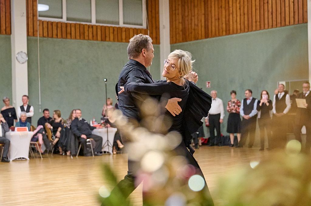 Tanzendes Paar in eleganter Kleidung auf einer Tanzfl&auml;che, umgeben von G&auml;sten in festlicher Atmosph&auml;re.