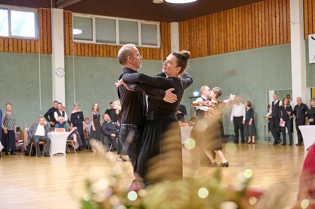 Tanzpaar in eleganter Kleidung f&uuml;hrt einen Walzer auf einer Tanzfl&auml;che vor einem Publikum aus mehreren Zuschauern aus.