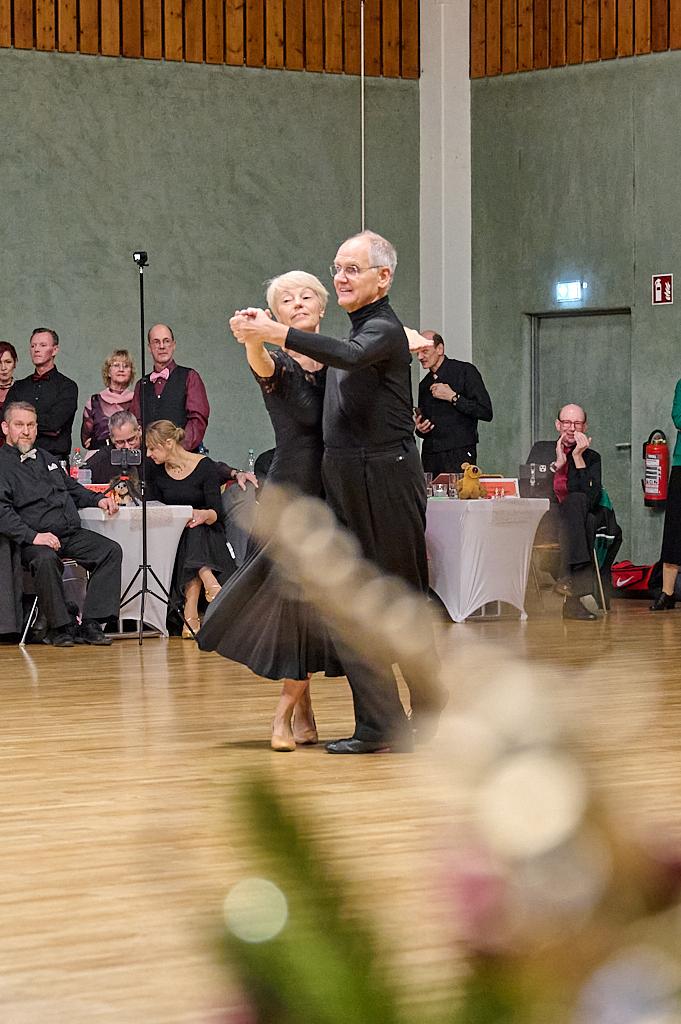Tanzpaar f&uuml;hrt einen Standardtanz auf einer Tanzfl&auml;che, umgeben von Zuschauern in festlicher Kleidung.