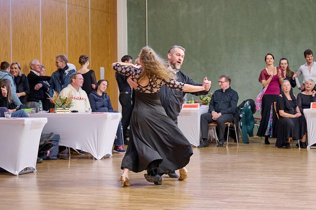 Tanzpaar in eleganter Kleidung f&uuml;hrt einen Tango in einem festlichen Saal mit Zuschauern im Hintergrund auf.