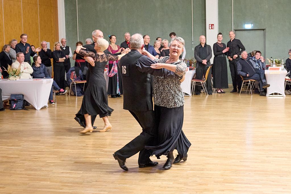 Tanzende Paare auf einer Tanzfl&auml;che, umgeben von Zuschauern in festlicher Kleidung. Atmosph&auml;rische Veranstaltung.