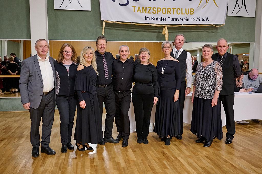 Gruppenfoto von zehn T&auml;nzern in festlicher Kleidung, im Hintergrund eine Tanzfl&auml;che und ein Banner des Tanzsportclubs.