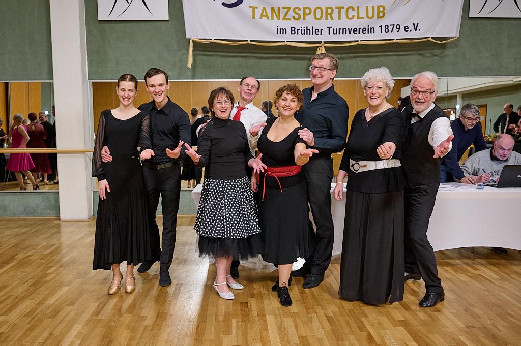 Gruppe von T&auml;nzern in eleganter Kleidung posiert l&auml;chelnd in einem Tanzsaal mit spiegelnden W&auml;nden.