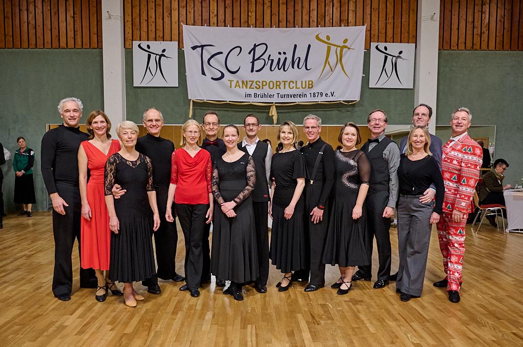 Gruppenfoto von T&auml;nzern in eleganter Kleidung vor dem Banner des TSC Br&uuml;hl im Tanzen.