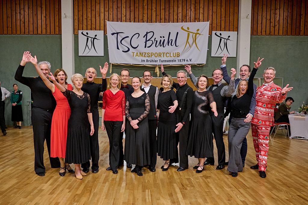 Gruppenshot von T&auml;nzern in festlicher Kleidung beim TSC Br&uuml;hl, vor einem Banner des Tanzsportclubs.
