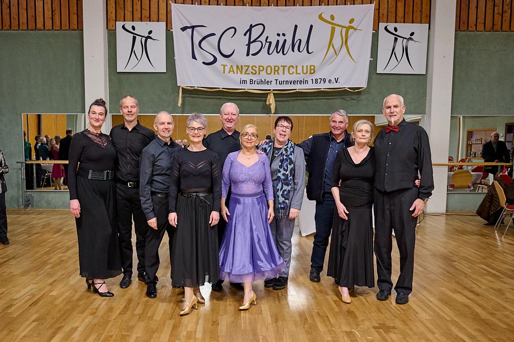 Gruppenfoto von 10 tanzenden Personen in eleganter Kleidung im TSC Br&uuml;hl Tanzenclub mit Banner im Hintergrund.