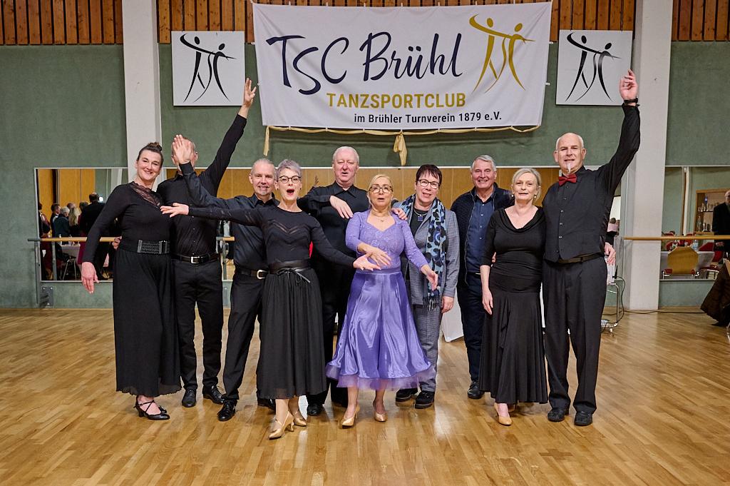 Gruppe von T&auml;nzern in eleganter Kleidung posiert vor einem Banner des TSC Br&uuml;hl im Tanzsportclub.