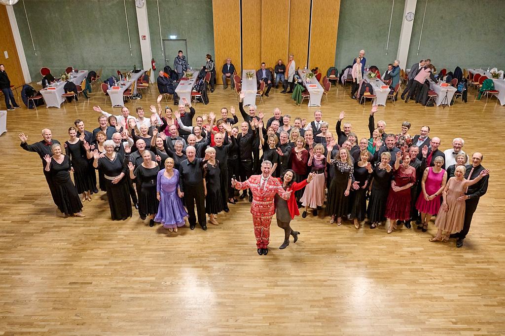 Gruppenaufnahme von Tanzenden in eleganter Kleidung, die jubelnd in einem festlich dekorierten Saal stehen.