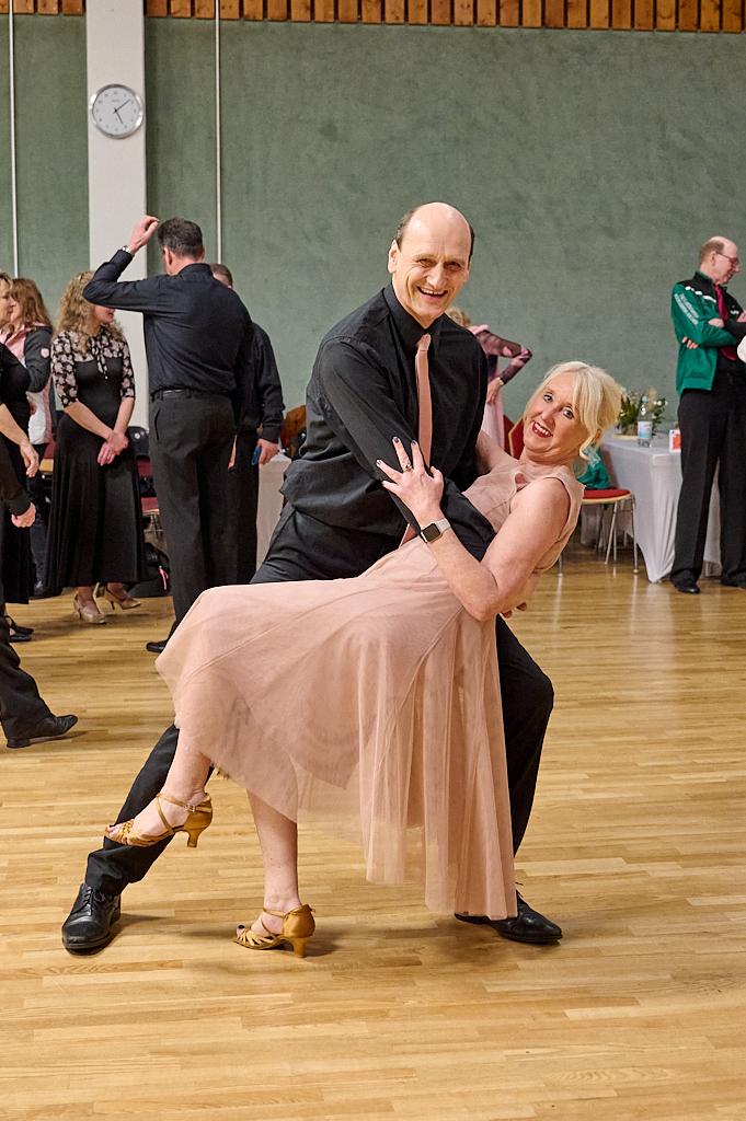 Tanzpaar in eleganter Kleidung f&uuml;hrt einen schwungvollen Schritt auf einer Tanzfl&auml;che aus Holz aus.