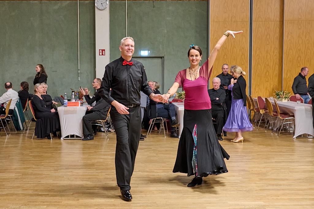 Tanzendes Paar in eleganter Kleidung auf der Tanzfl&auml;che, umgeben von G&auml;sten in einem festlichen Saal.