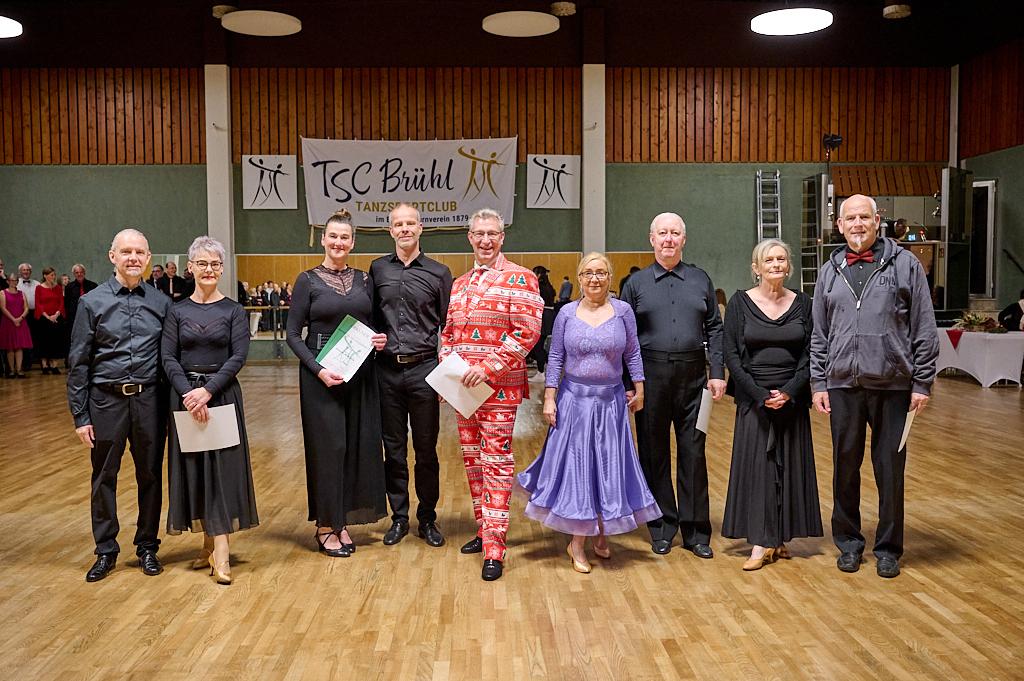 Gruppe von T&auml;nzern in eleganter Kleidung steht auf einer Tanzfl&auml;che, mit Urkunden in der Hand und einem Banner im Hintergrund.