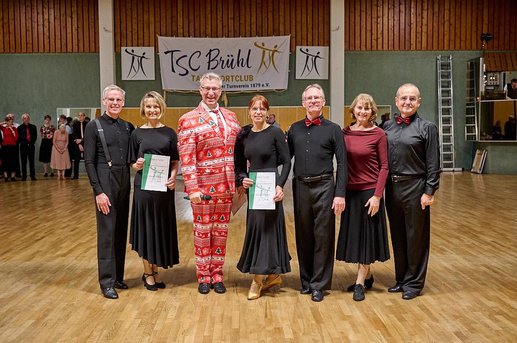 Gruppe von T&auml;nzern in formeller Kleidung, die Preistr&auml;ger mit Urkunden in einer Tanzhalle des TSC Br&uuml;hl sind.