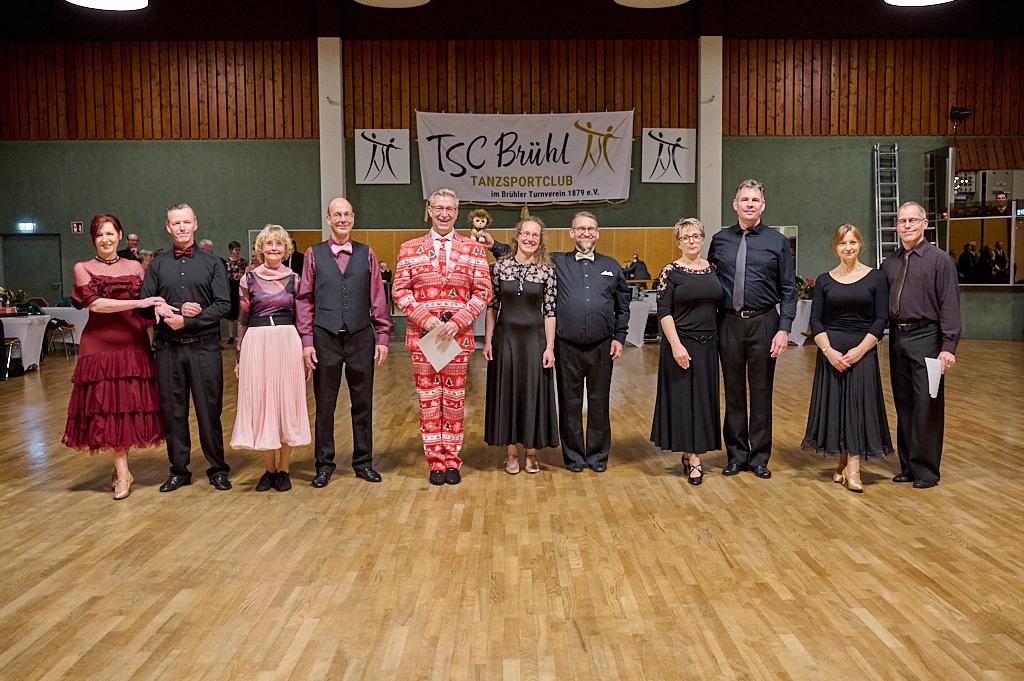 Gruppe von T&auml;nzern in eleganter Kleidung auf einer Tanzfl&auml;che mit Vereinsbanner im Hintergrund.