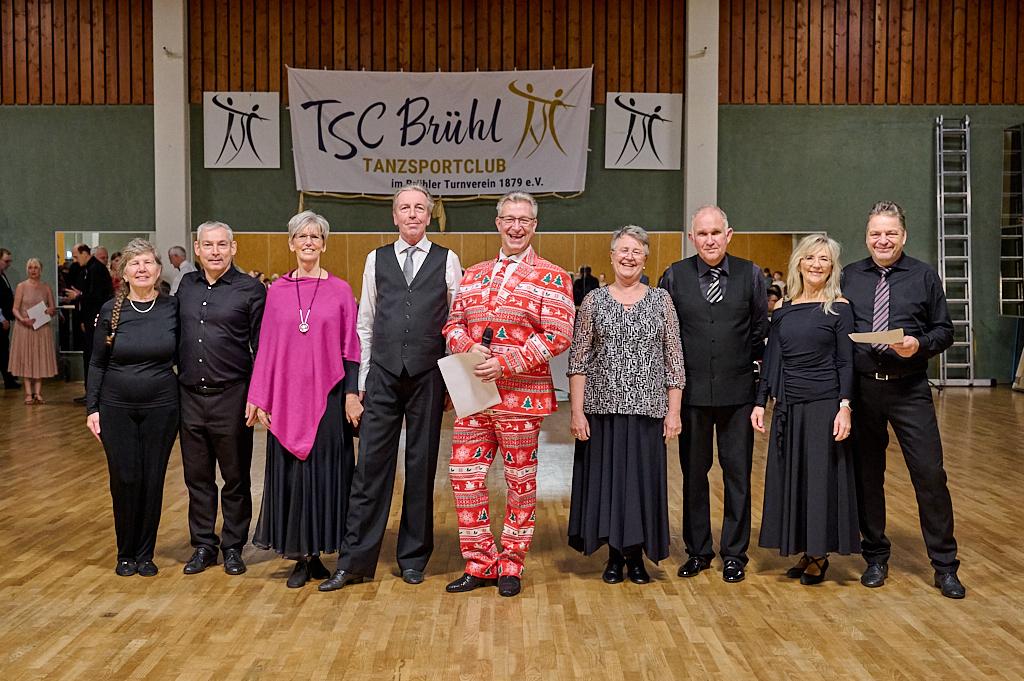 Gruppenfoto von T&auml;nzern in festlicher Kleidung im TSC Br&uuml;hl Tanzsportclub, vor einem Veranstaltungsbanner.