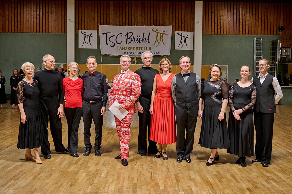 Eine Gruppe von T&auml;nzern in festlicher Kleidung steht auf einer Tanzfl&auml;che vor einem Banner des TSC B&uuml;hhl.
