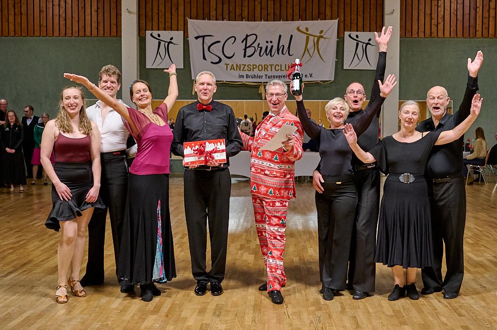 Gruppe von T&auml;nzern in festlicher Kleidung, die strahlend auf einer Tanzfl&auml;che zusammen feiern. Banner im Hintergrund.