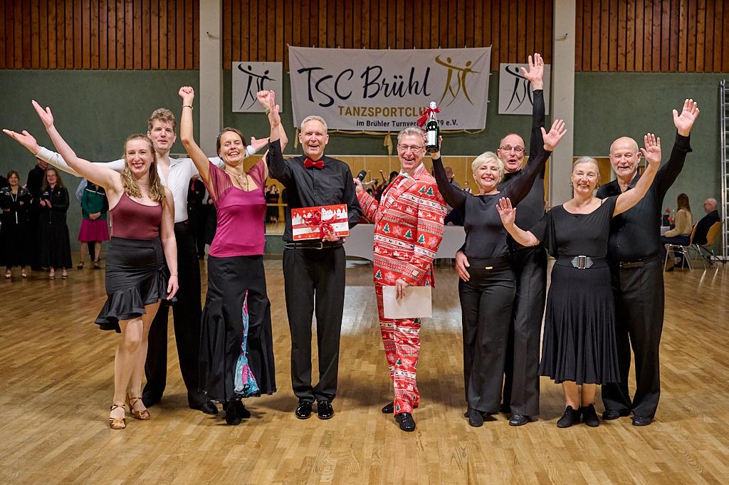 Gruppenszene von tanzenden Personen im Festkleid auf einer Tanzveranstaltung im TSC Br&uuml;hl, alle mit freudigen Gesten.