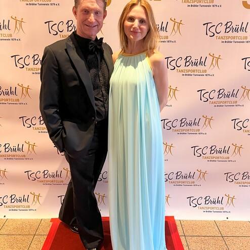 Paar in festlicher Kleidung steht vor einem Banner zum 50-jährigen Jubiläum des TSC Brühl.