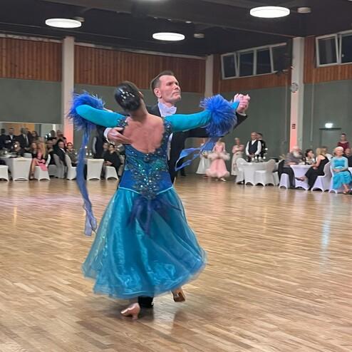 Tanzpaar in eleganter Kleidung mit fließendem Rock und Rüschen tanzt in einem festlichen Saal.