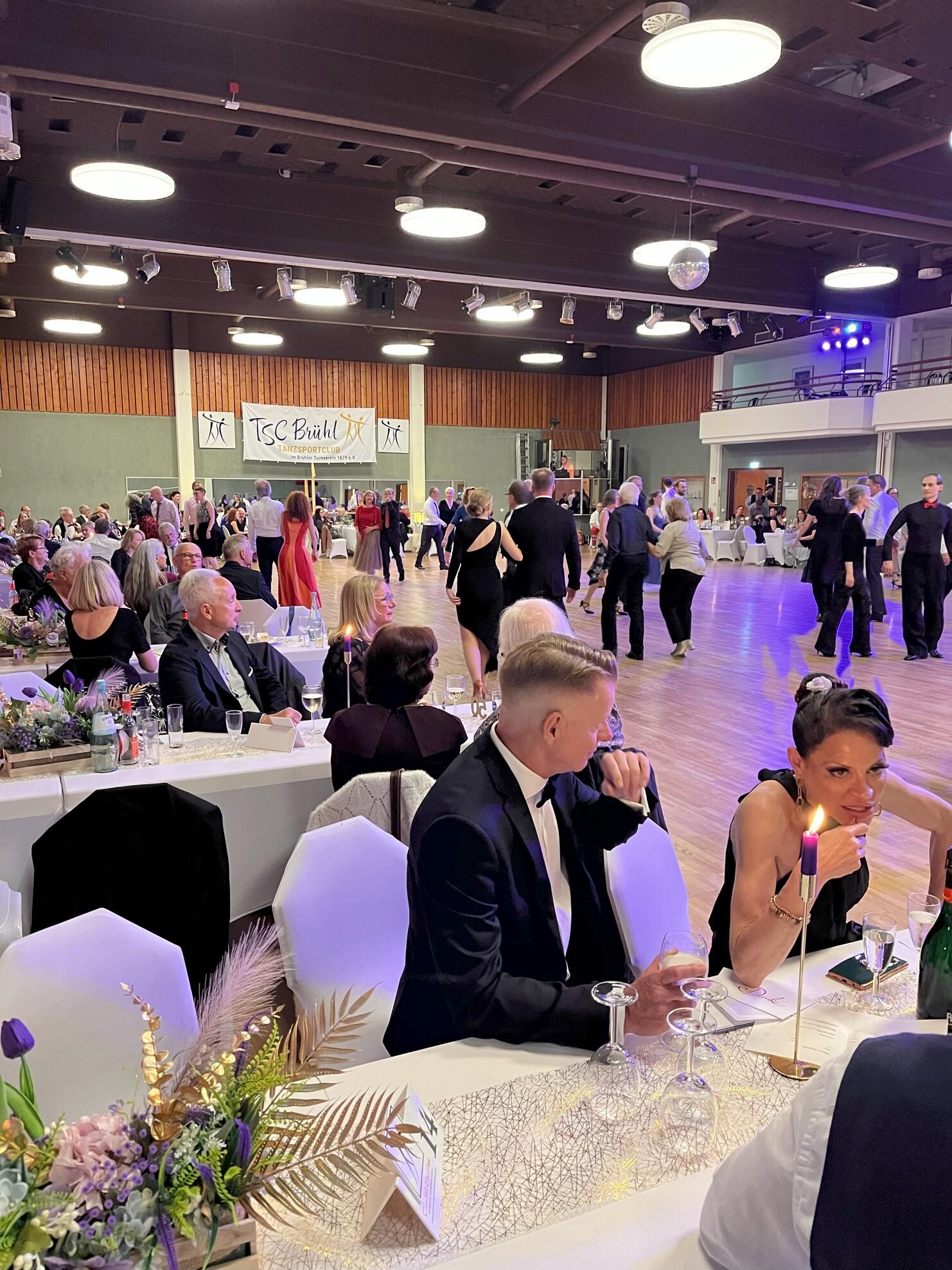 Tanzveranstaltung im TSC Bühl: Paare tanzen auf der Fläche, Gäste sitzen an festlich gedeckten Tischen.