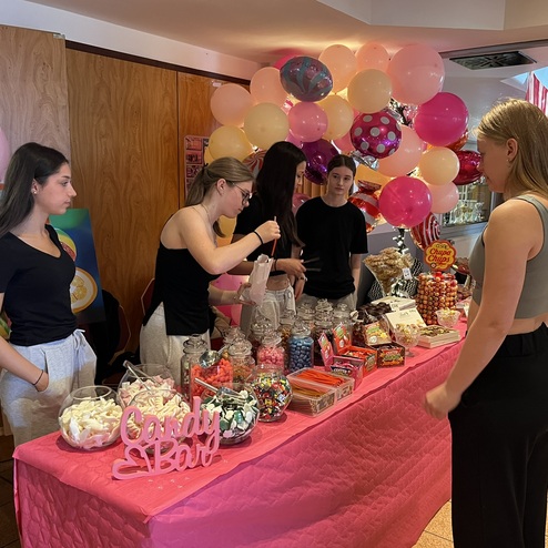 Bunte S&uuml;&szlig;igkeiten und Snacks an einem dekorierten Candy-Buffet mit Studenten in einem festlichen Raum.