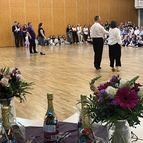 Tanzvorf&uuml;hrung in einem Festsaal mit Publikum, Fokus auf tanzendes Paar und Blumendekoration auf einem Tisch.