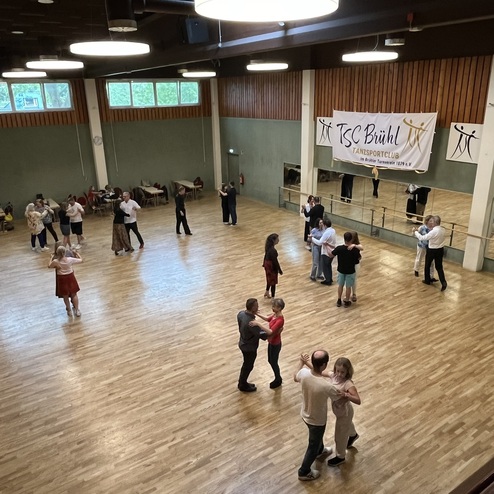 Tanzende Paare in einem gro&szlig;en Saal mit Holzfu&szlig;boden, Spiegeln und Banner des TSC B&uuml;hl.
