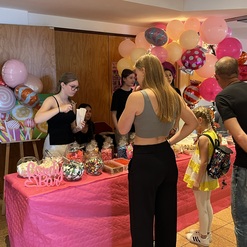 Bunte Candy-Bar mit S&uuml;&szlig;igkeiten und G&auml;sten, darunter ein Kind in gelbem Outfit und Luftballons im Hintergrund.