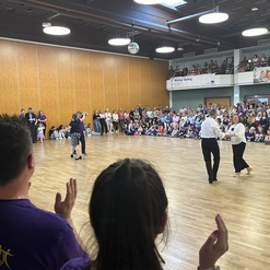 Tanzpaar in eleganter Kleidung f&uuml;hrt eine Darbietung vor einer gro&szlig;en, applaudierender Zuschauermenge in einem Saal.