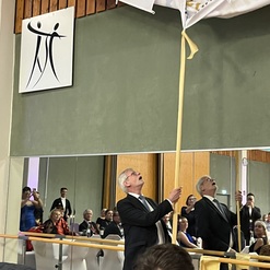 Zwei M&auml;nner in Anz&uuml;gen ziehen an einem Banner in einem festlich dekorierten Raum mit G&auml;sten.