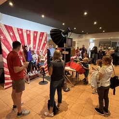 Gruppenkinder posieren vor einem rot-wei&szlig; gestreiften Hintergrund, w&auml;hrend Erwachsene in einer belebten Veranstaltungshalle zuschauen.