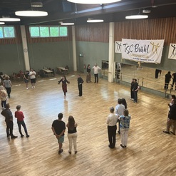 Tanztraining im TSC Br&uuml;hl mit mehreren Teilnehmern auf einer Holzparkettfl&auml;che und einem Banner im Hintergrund.