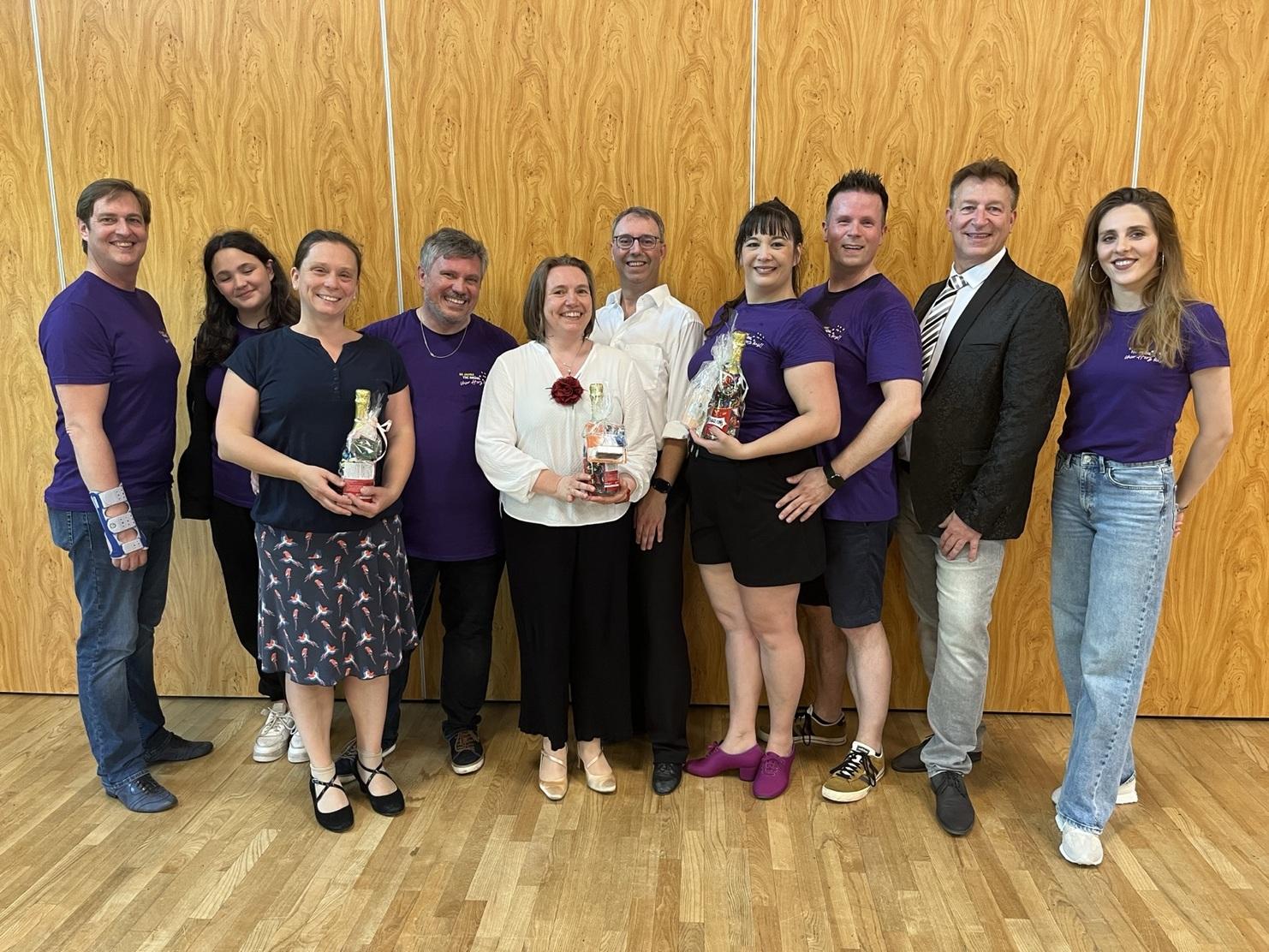 Gruppenportrait von zehn Personen in lila T-Shirts, die Geschenke in der Hand halten, vor einer Holzverkleidung.