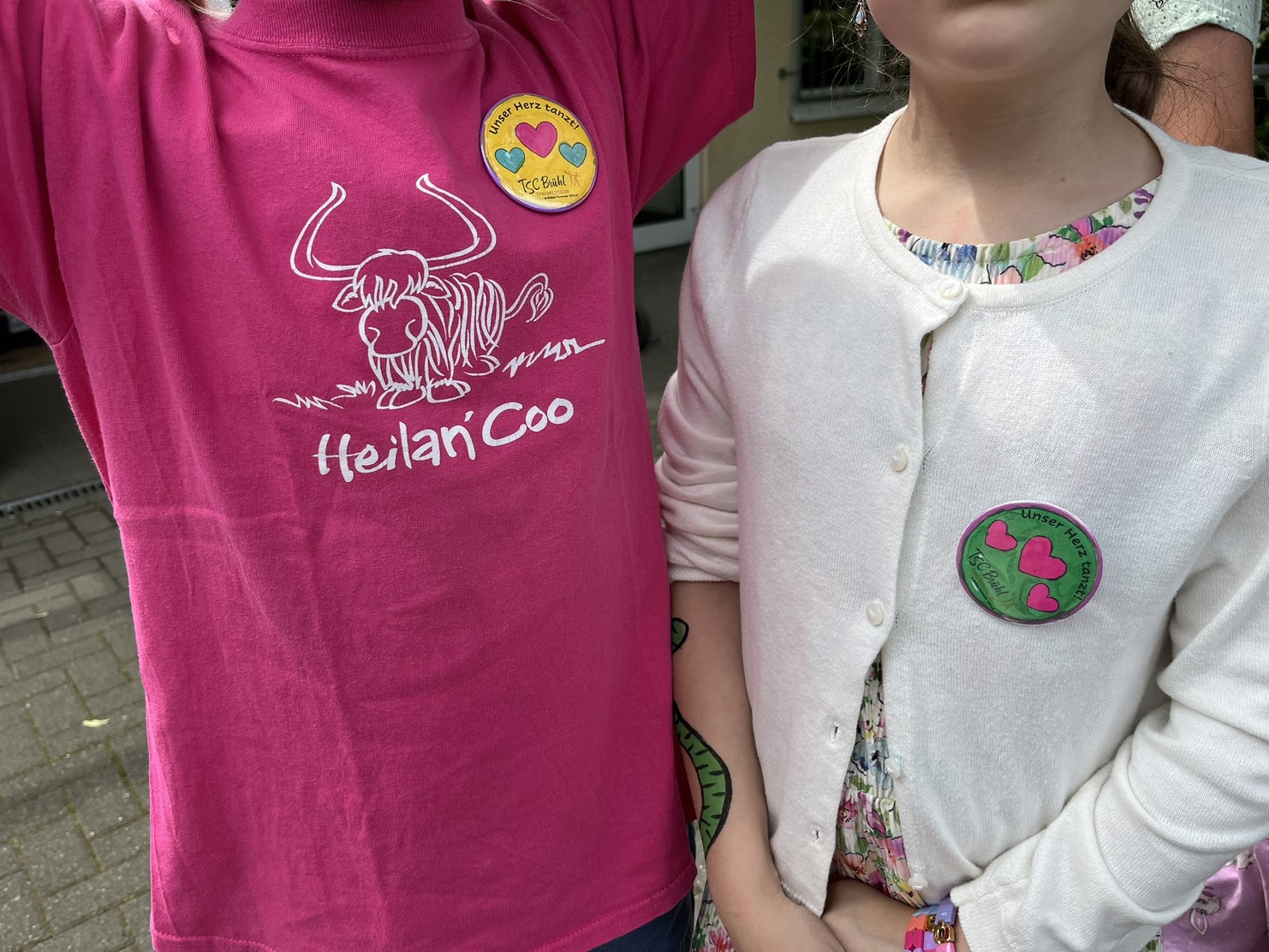 Zwei Kinder mit einem pinken T-Shirt und einem wei&szlig;en Cardigan, jeweils mit bunten Ansteckern.