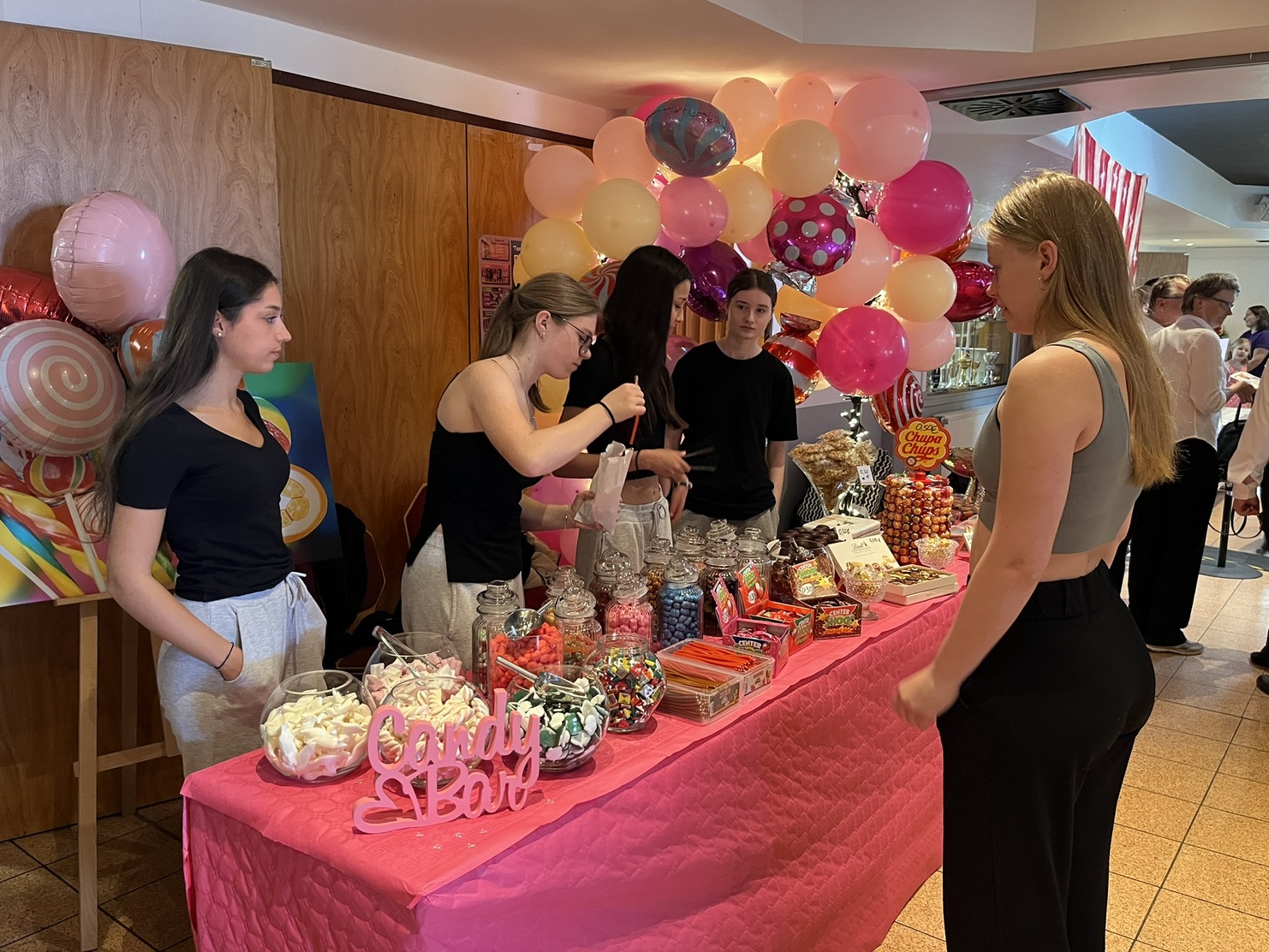 Bunte S&uuml;&szlig;igkeiten und Snacks an einem dekorierten Candy-Buffet mit Studenten in einem festlichen Raum.