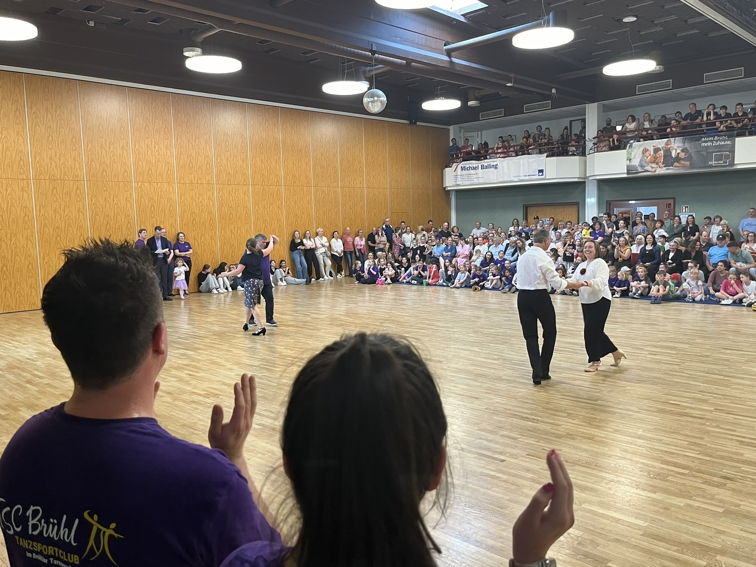 Tanzpaar in eleganter Kleidung f&uuml;hrt eine Darbietung vor einer gro&szlig;en, applaudierender Zuschauermenge in einem Saal.