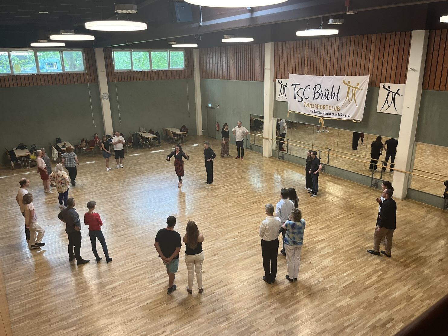 Tanztraining im TSC Br&uuml;hl mit mehreren Teilnehmern auf einer Holzparkettfl&auml;che und einem Banner im Hintergrund.