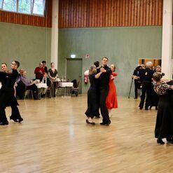 Tanzende Paare in eleganter Kleidung auf einer Tanzfl&auml;che, umgeben von Zuschauern an Tischen.